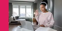A woman with headphones waving at a laptop