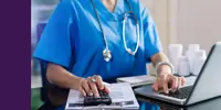 A healthcare worker using a laptop and a calculator